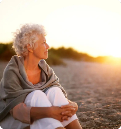 A woman sitting on the beach looking out at the sunset.