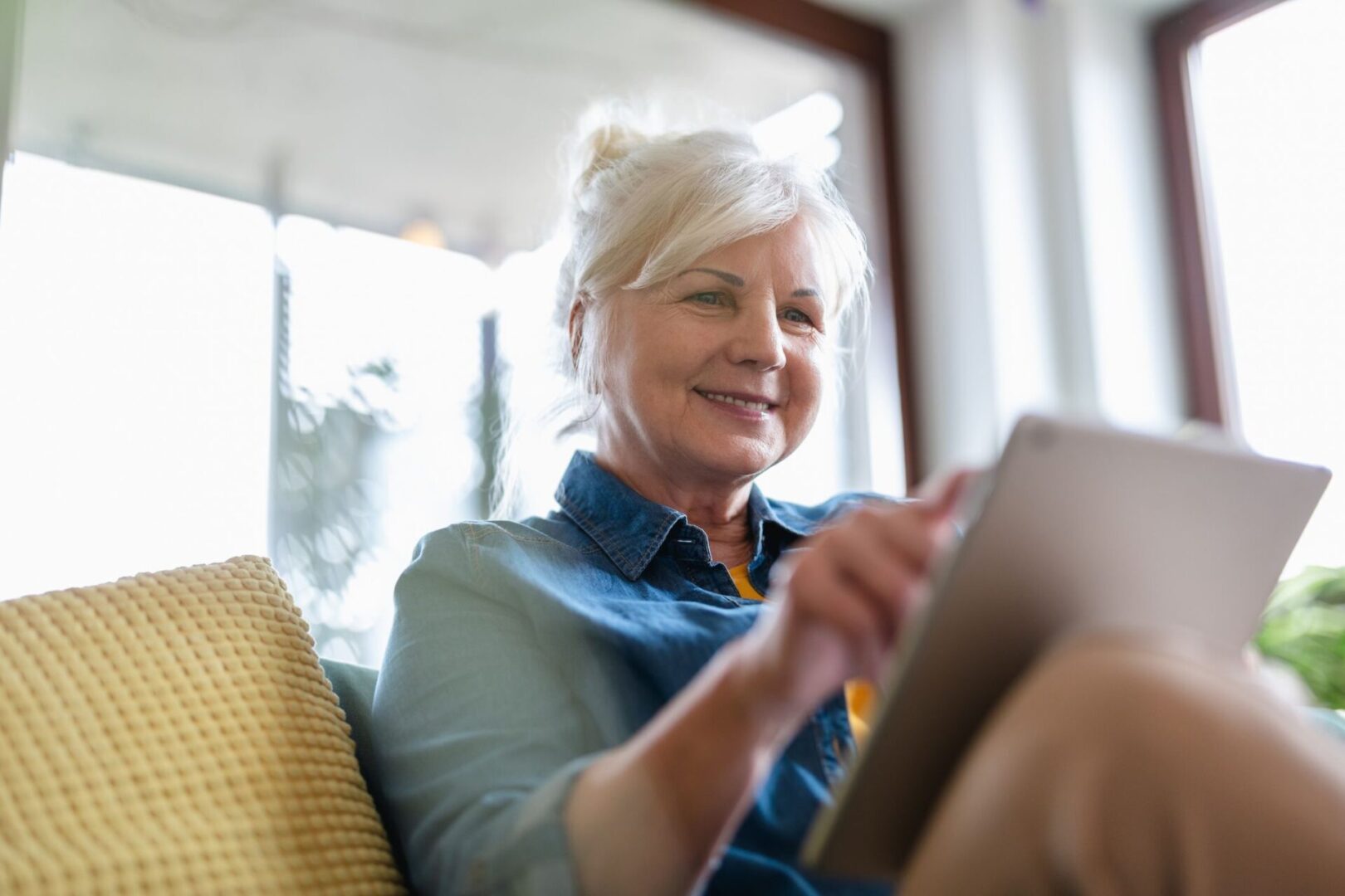 A woman sitting on the couch looking at her tablet.